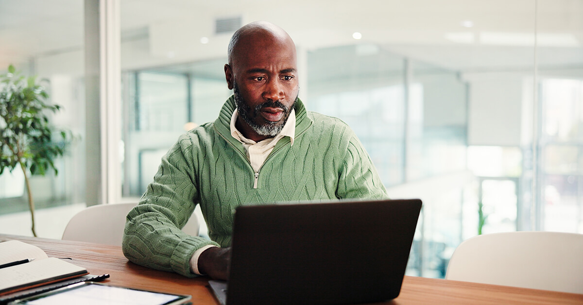Focused professional looking concerned while working on a laptop at a desk in a modern office setting.