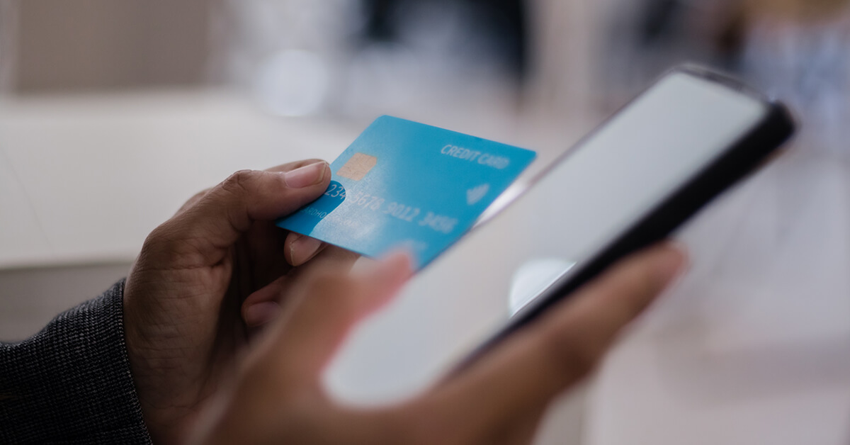 Person holding a credit card while using a smartphone for an online payment.