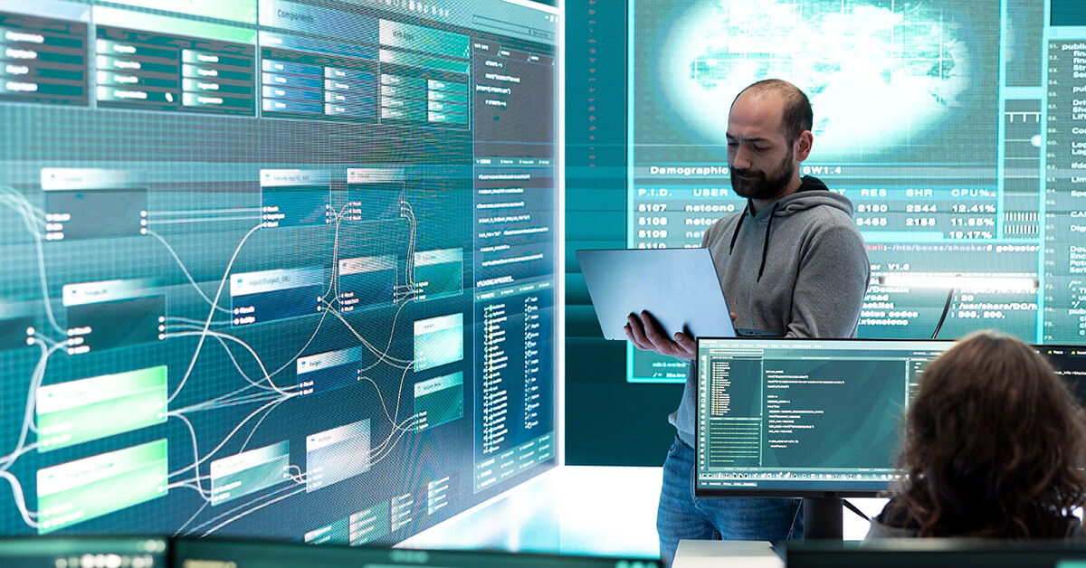 IT specialist analyzing cloud environment architecture and service relationships on large monitoring displays.