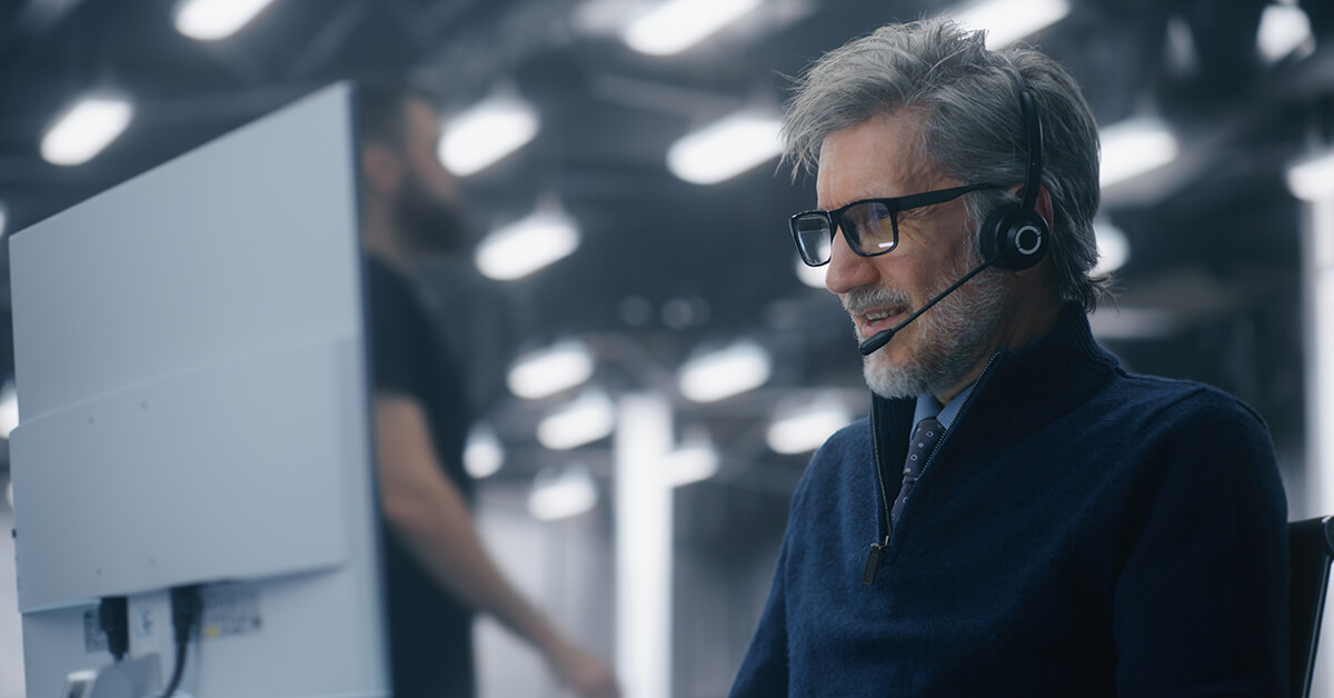 Senior IT professional wearing headset at workstation.