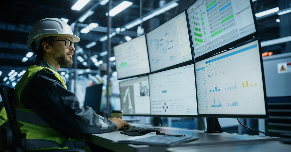 Manufacturing engineer monitoring production systems and operational technology on multiple screens.