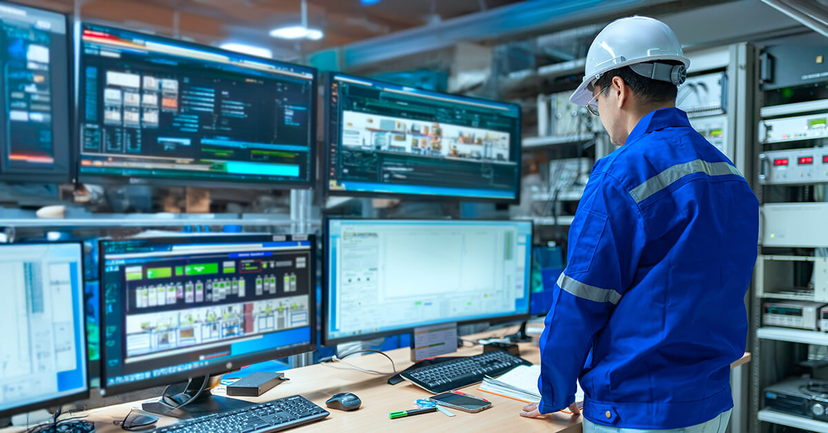 Industrial technician connecting a laptop to operational technology equipment on a factory floor.
